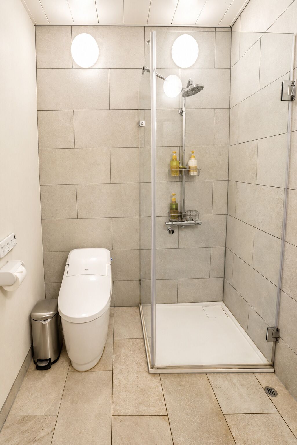 Un baño moderno con ducha envuelta en vidrio, inodoro y un cubo de basura.