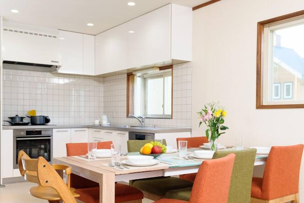 Een moderne keuken met witte kasten, een eettafel met oranje stoelen en een fruitschaal op tafel.
