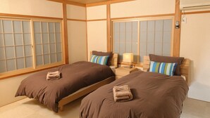 A traditional Japanese-style room with two beds, wooden flooring, sliding shoji doors, and a ceiling fan.
