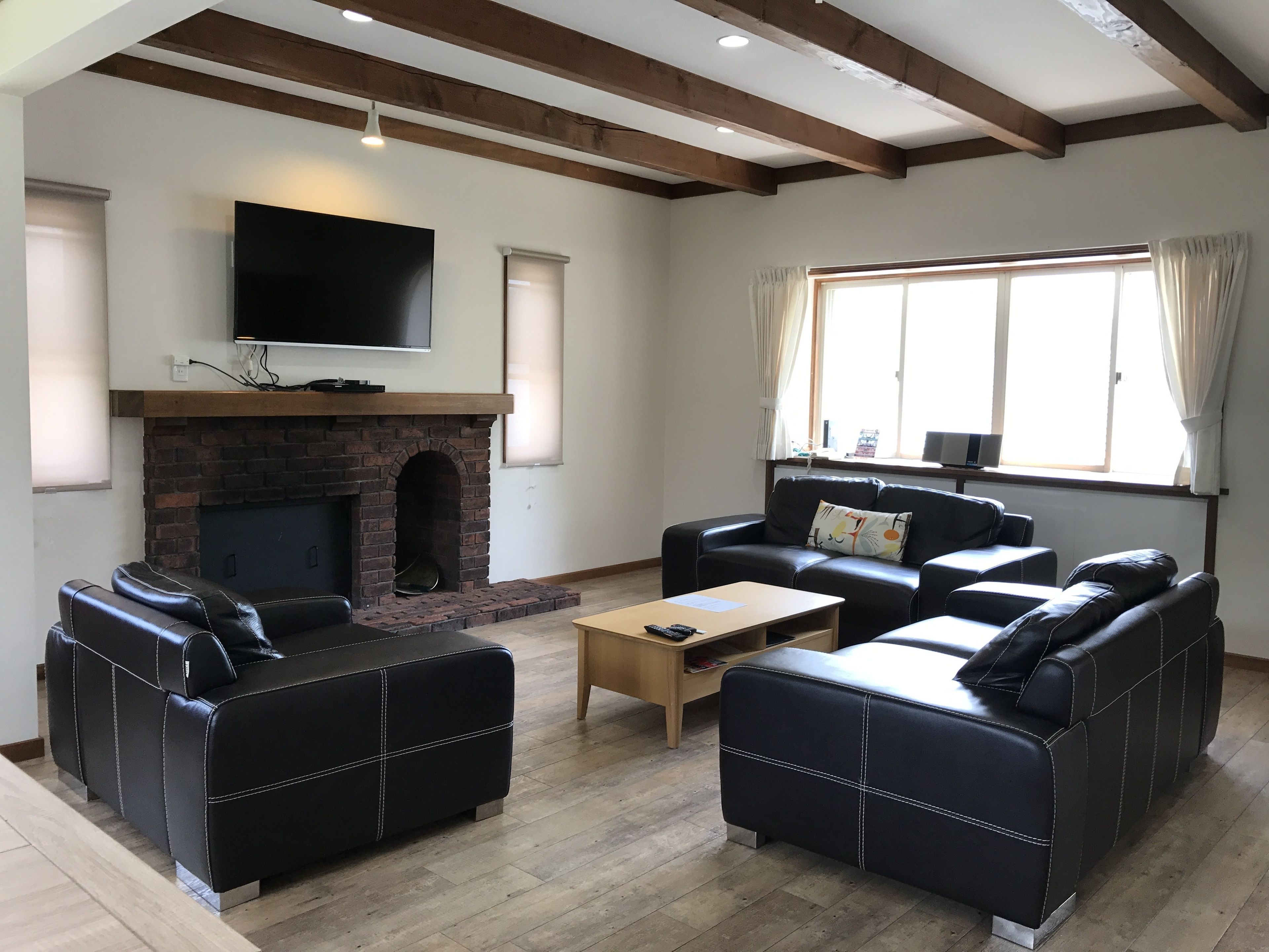 A spacious living room with a fireplace, leather sofas, a coffee table, and a large TV mounted on the wall.