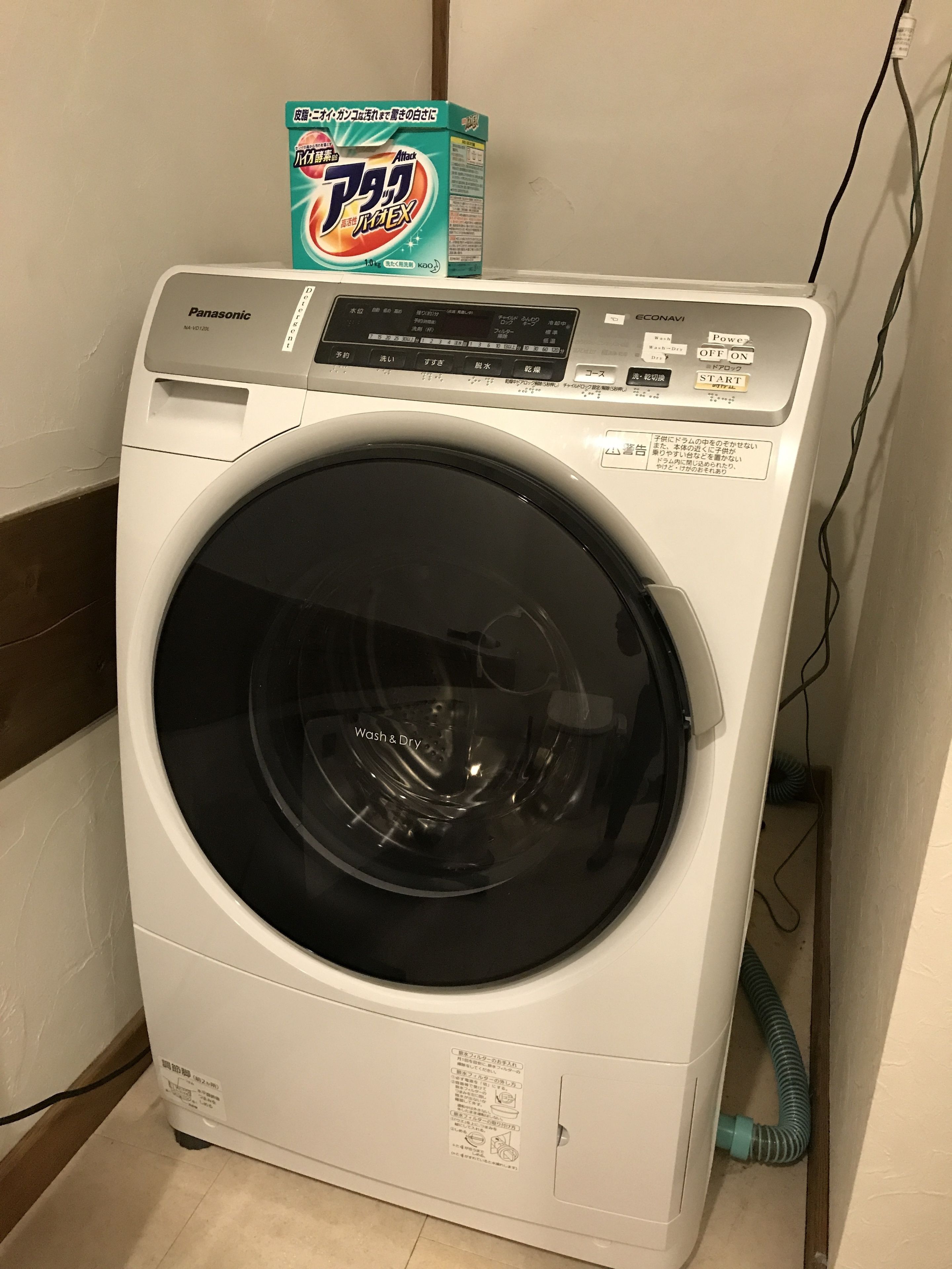 Une machine à laver à chargement frontal, dotée d’un panneau de commande, d’un compartiment à lessive et d’un câble d’alimentation.