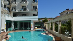 A swimming pool with a sun deck, lounge chairs, and a view of a hillside. - Kalif Hotel (Ayvalik)