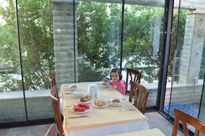 A dining table with food and a child seated at it, overlooking a garden. - Kalif Hotel (Ayvalik)