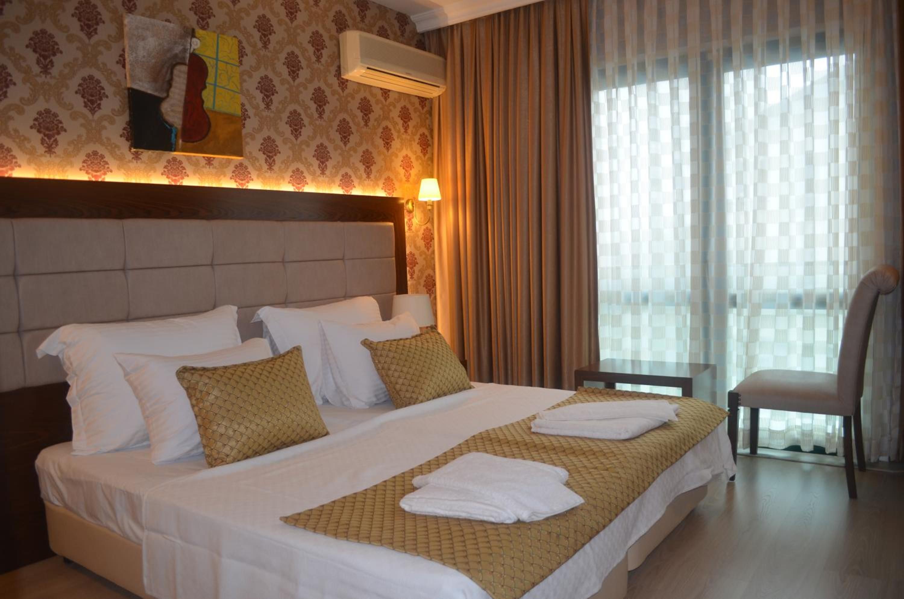 Ein Hotelzimmer mit einem großen Bett, einem Kopfteil, einem Nachttisch, einem Sessel und einem Fenster mit Vorhängen.