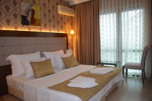 A hotel room with a large bed, a headboard, a bedside table, a chair, and a window with curtains. - Kalif Hotel (Ayvalik)