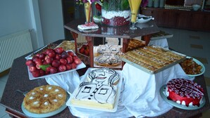 A table with various desserts and fruits, including a cake with a face design, a red cake, and a tray of strawberries. - Kalif Hotel (Ayvalik)
