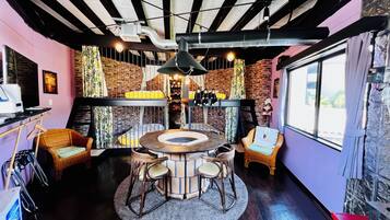A cozy room with a round table, wicker chairs, a brick wall, and a large window.