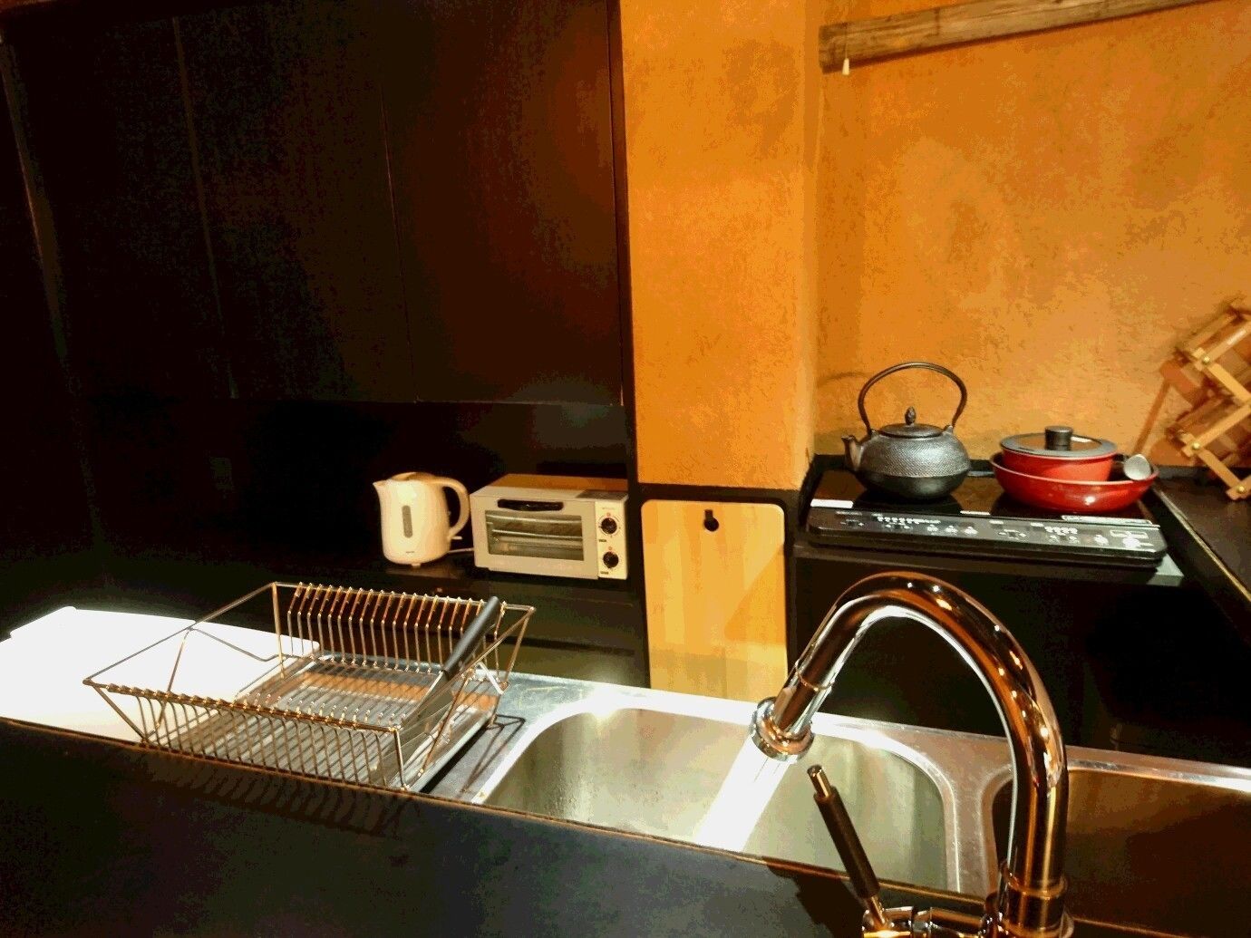 Uma cozinha com uma pia de aço inoxidável, chaleira, torradeira e uma panela vermelha no fogão.