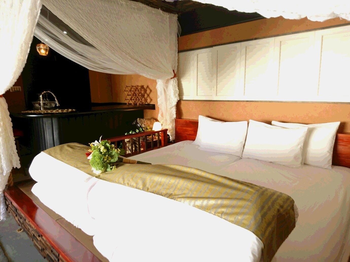 Una habitación de hotel con una cama, cortinas blancas, una mesita de noche y un jarrón con flores.