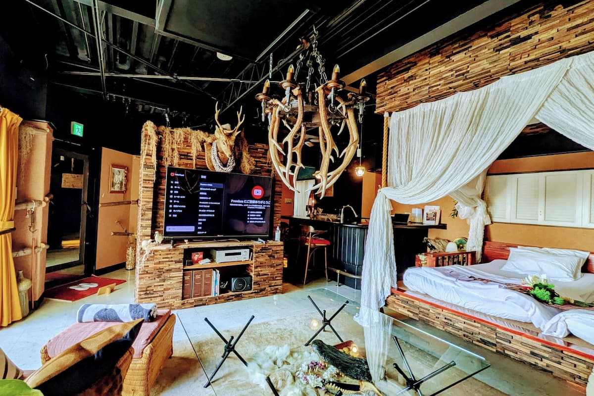 A room with a bed, a television, a wooden wall, and a chandelier.
