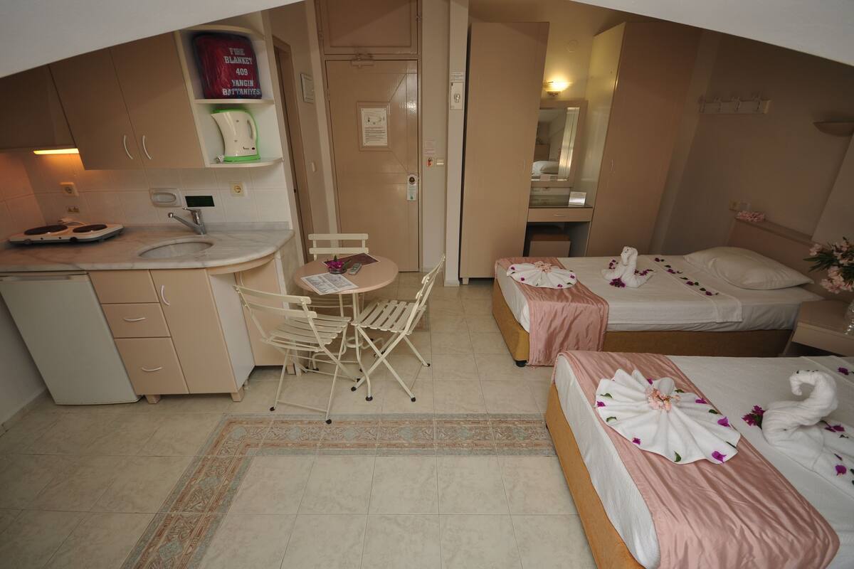 A hotel room with a kitchenette, a dining area with a table and chairs, two beds with floral decorations, and a bathroom visible through an open door.