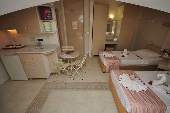 A hotel room with a kitchenette, a dining area with a table and chairs, two beds with floral decorations, and a bathroom visible through an open door.