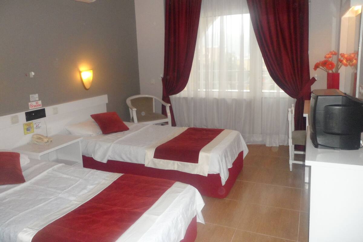 A hotel room with two beds, a desk, a chair, a TV, and a window with curtains.