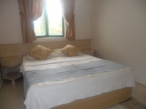 A bedroom with a bed, two pillows, a nightstand, a window with curtains, and a bedside table. - Club Atrium Marmaris (Marmaris)