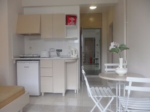 A compact kitchen with a refrigerator, a coffee maker, and a microwave. There is a dining area with a white table and chairs, and a vase with flowers on the table. - Club Atrium Marmaris (Marmaris)