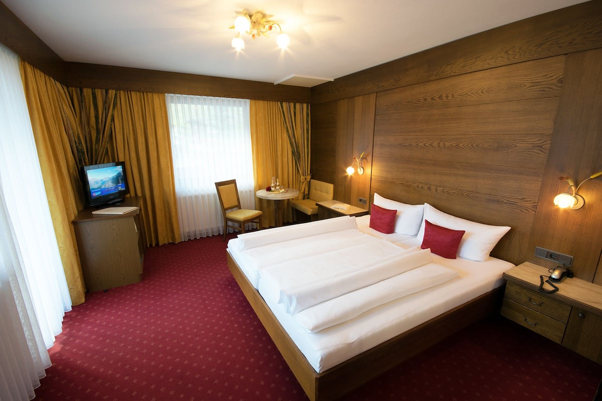 A hotel room with a large bed, a desk with a chair, a television, and a small table with a lamp.