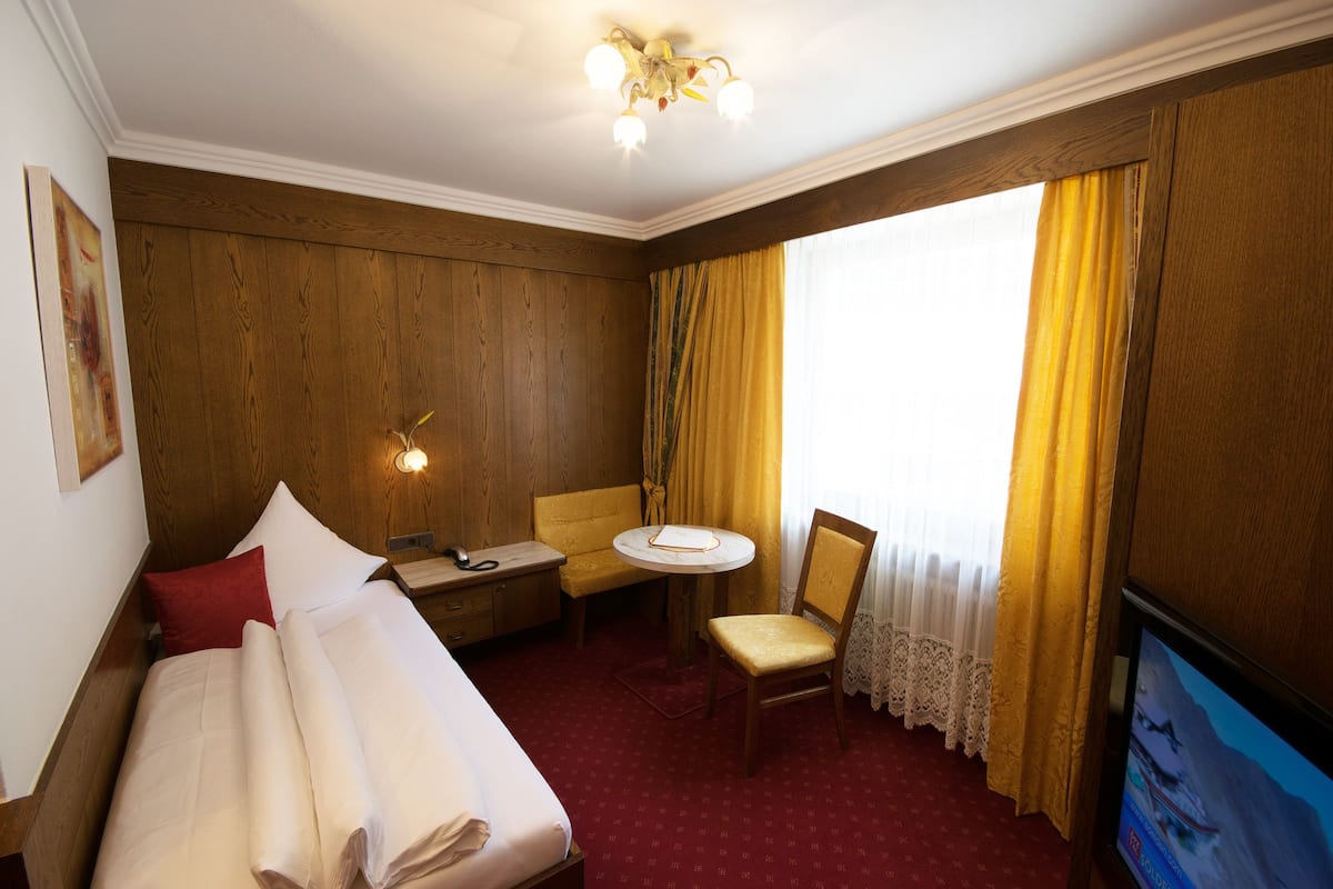 A hotel room with a bed, a small table, a chair, a television, and a window with curtains.