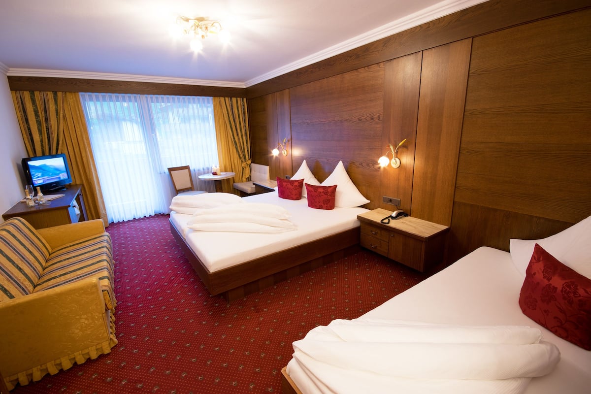 A hotel room with a large bed, a sofa, a TV, and a desk with a lamp.