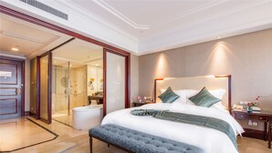 A hotel room with a large bed, a bench, a nightstand, and a bathroom visible through an open door. - Qianjiang Junting Hotel, Haining (Jiaxing)