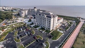 A large hotel with multiple buildings, a parking lot, and a waterfront view. - Qianjiang Junting Hotel, Haining (Jiaxing)