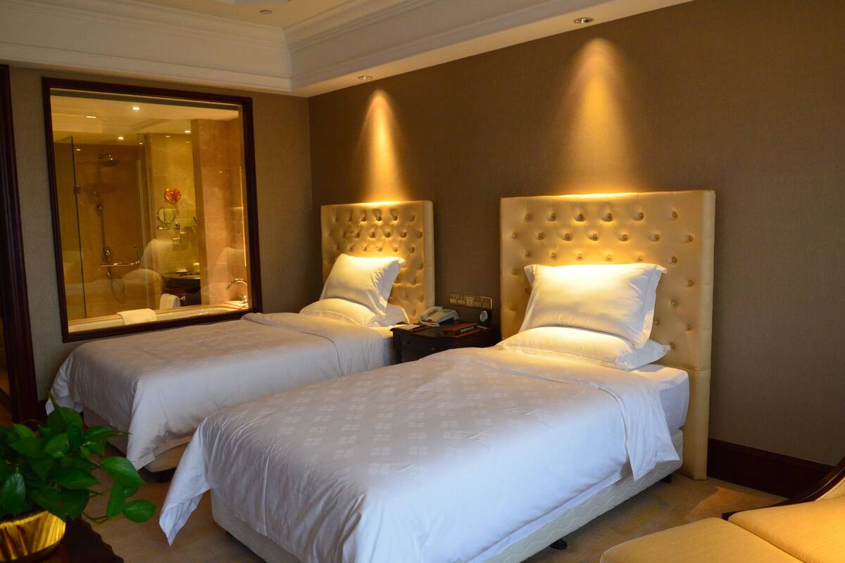 A hotel room with two beds, a large mirror, and a nightstand with a lamp.