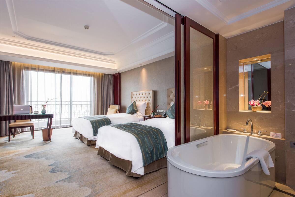 A hotel room with two beds, a desk, a laptop, a large bathtub, and a mirror.