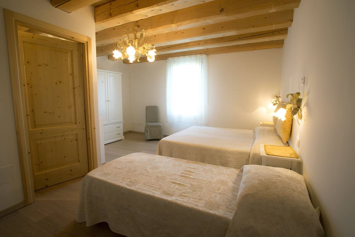 A bedroom with two beds, a wooden door, a wardrobe, and a chandelier.
