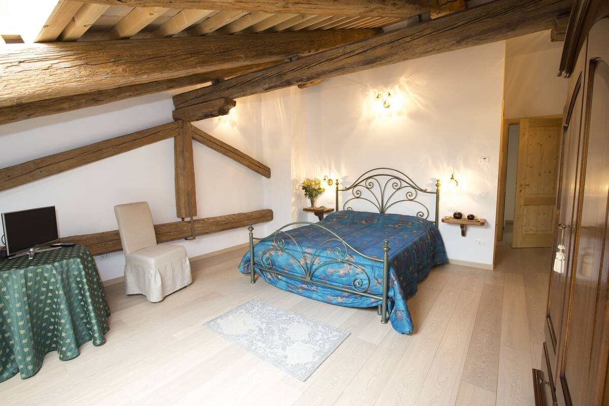 A bedroom with a bed, a desk, a chair, and a wooden ceiling.
