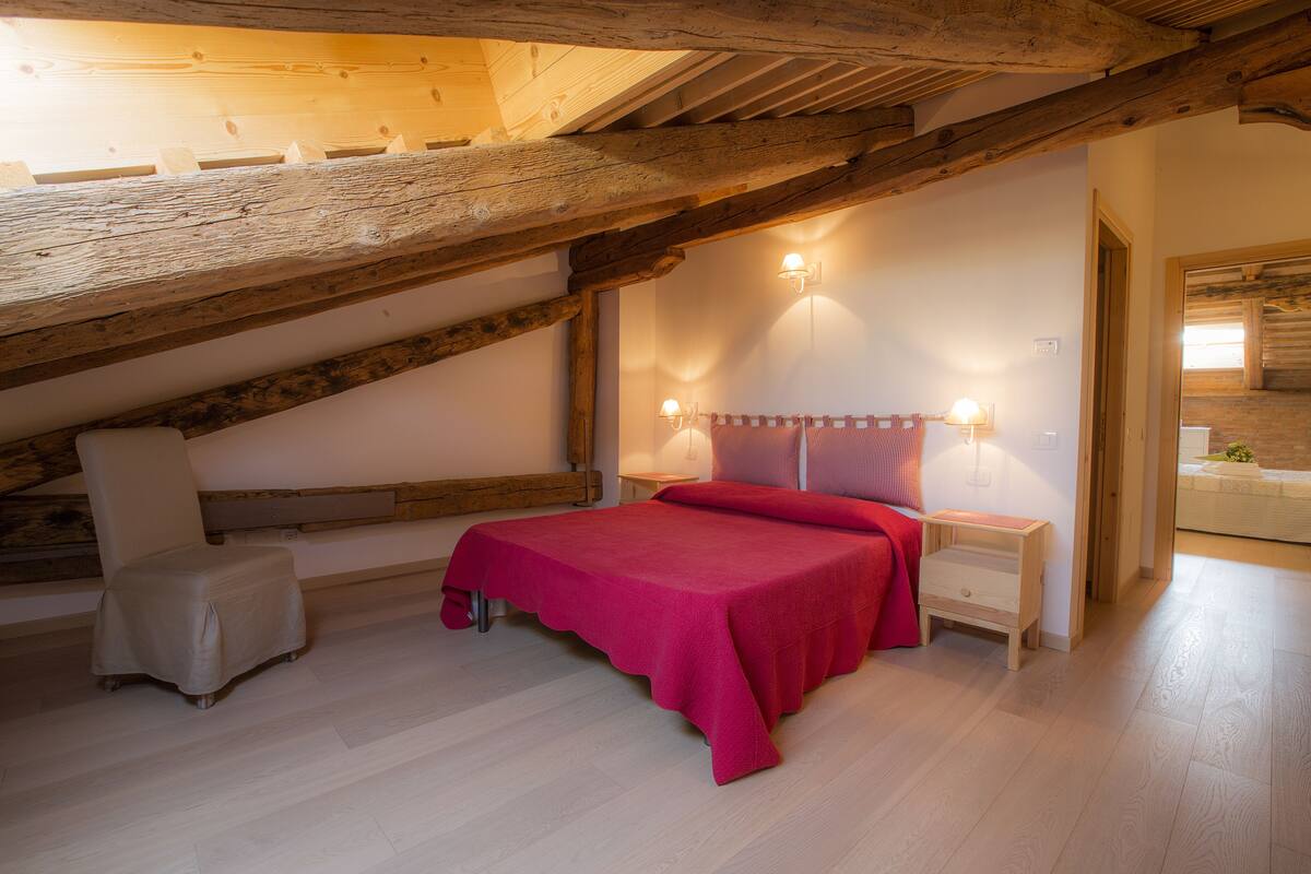 A bedroom with a bed, a nightstand, a chair, and a wooden ceiling.