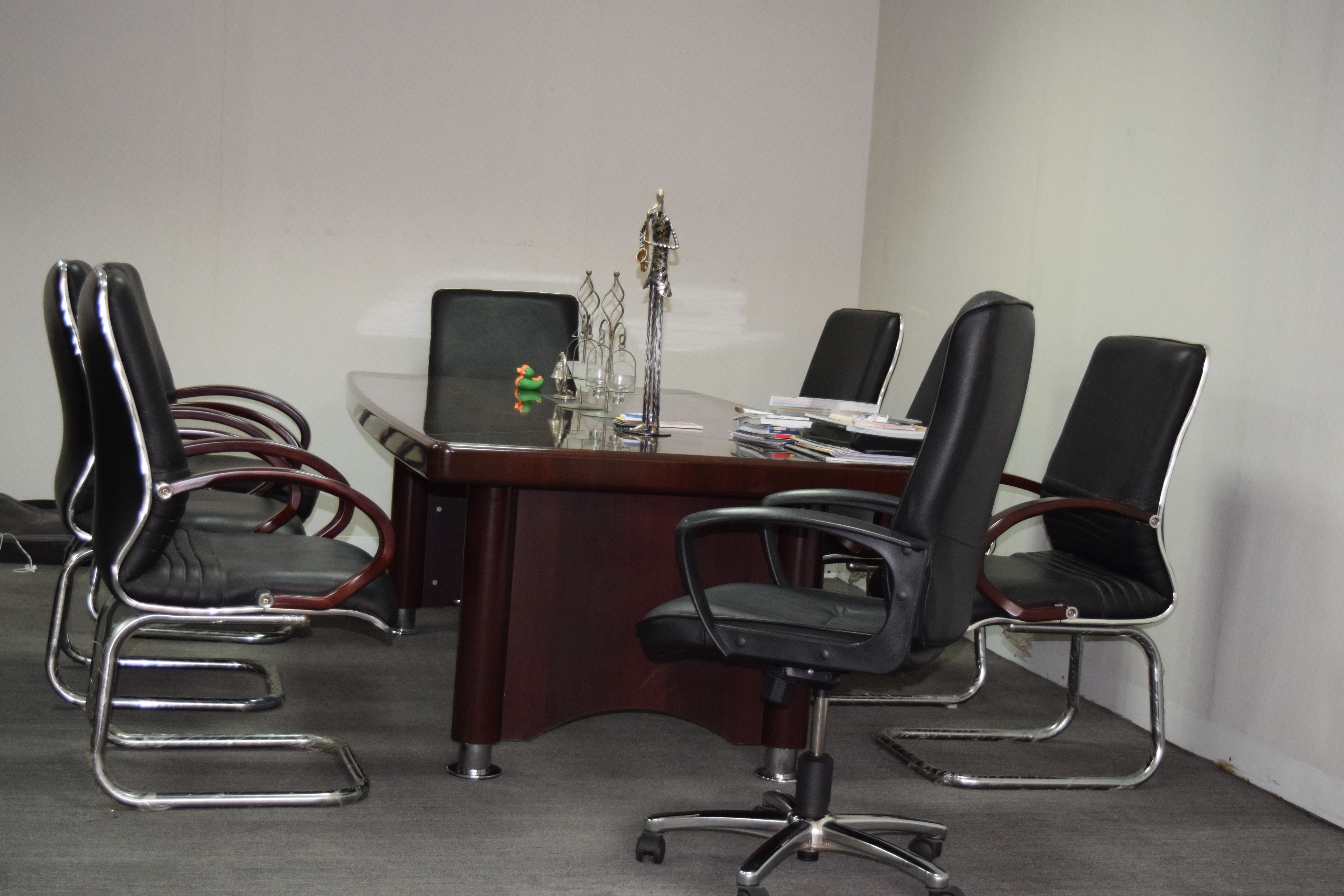 A conference room with a wooden table, four black office chairs, and a glass-top table.