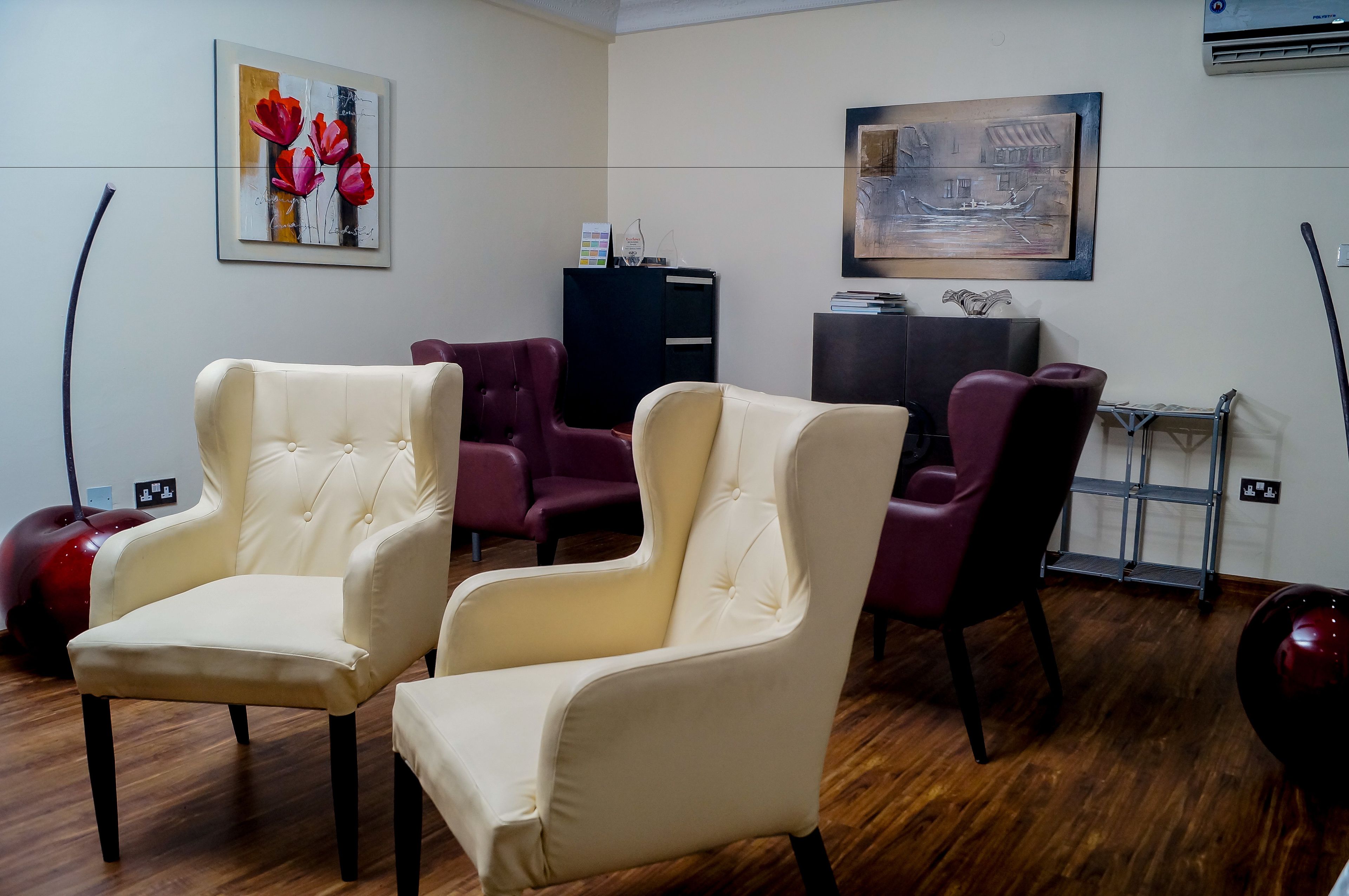 A room with two cream-colored armchairs, a black cabinet, and a red sofa.