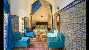 A room with a bed, two blue armchairs, a patterned wall, and a decorative archway. - Riad Dar Jabador (Salé)
