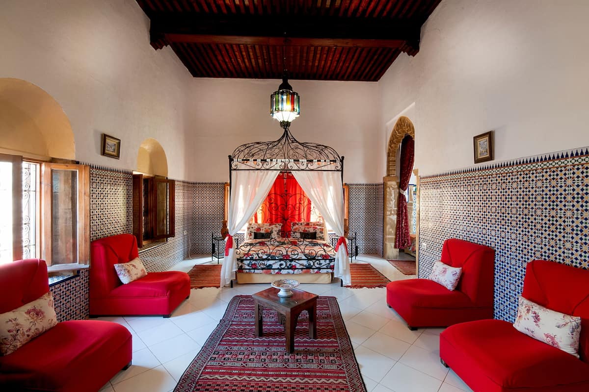 Une pièce avec un lit, des canapés rouges, un tapis à motifs et un lustre décoratif.