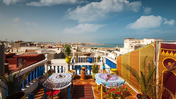 A rooftop terrace with a view of the city and sea, featuring patterned umbrellas and potted plants. - Riad Dar Jabador (Salé)