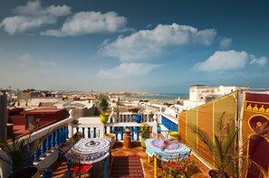 A rooftop terrace with a view of the city and sea, featuring patterned umbrellas and potted plants. - Riad Dar Jabador (Salé)