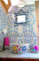 Un baño con un lavamanos grande con motivos florales, un espejo y azulejos estampados.