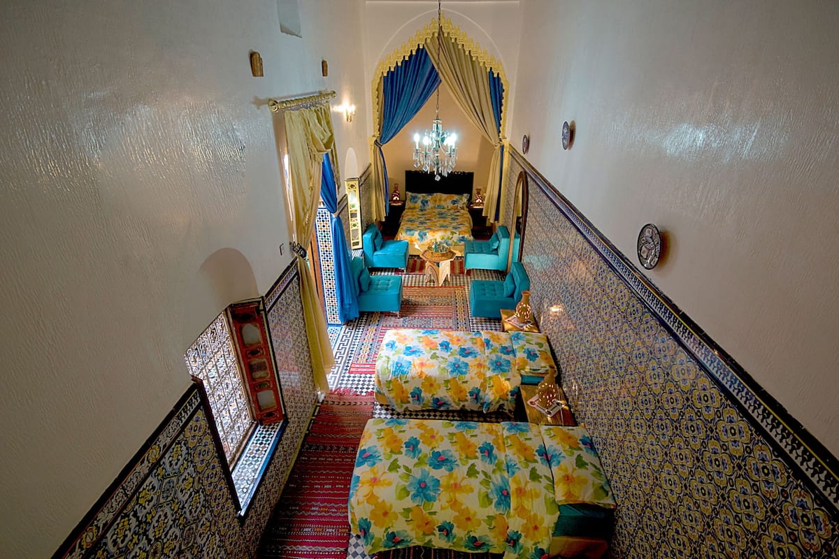 Un escalier étroit mène à une chambre à coucher dotée d’un lit à baldaquin, de deux fauteuils et d’un lustre.