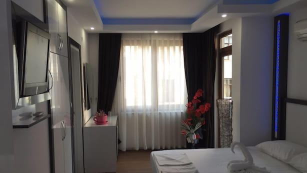 A hotel room with a bed, a TV, a desk, and a window with curtains. - Copenhagen Hotel (Alanya)