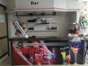 A bar area at Copenhagen Hotel with a sign indicating it's a bar, shelves with glasses and bottles, and a banner with the hotel's name and a cocktail image. - Copenhagen Hotel (Alanya)