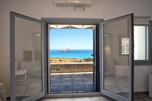 Una habitación con un amplio ventanal corredera que da a un balcón con vistas al mar y un paisaje rocoso.