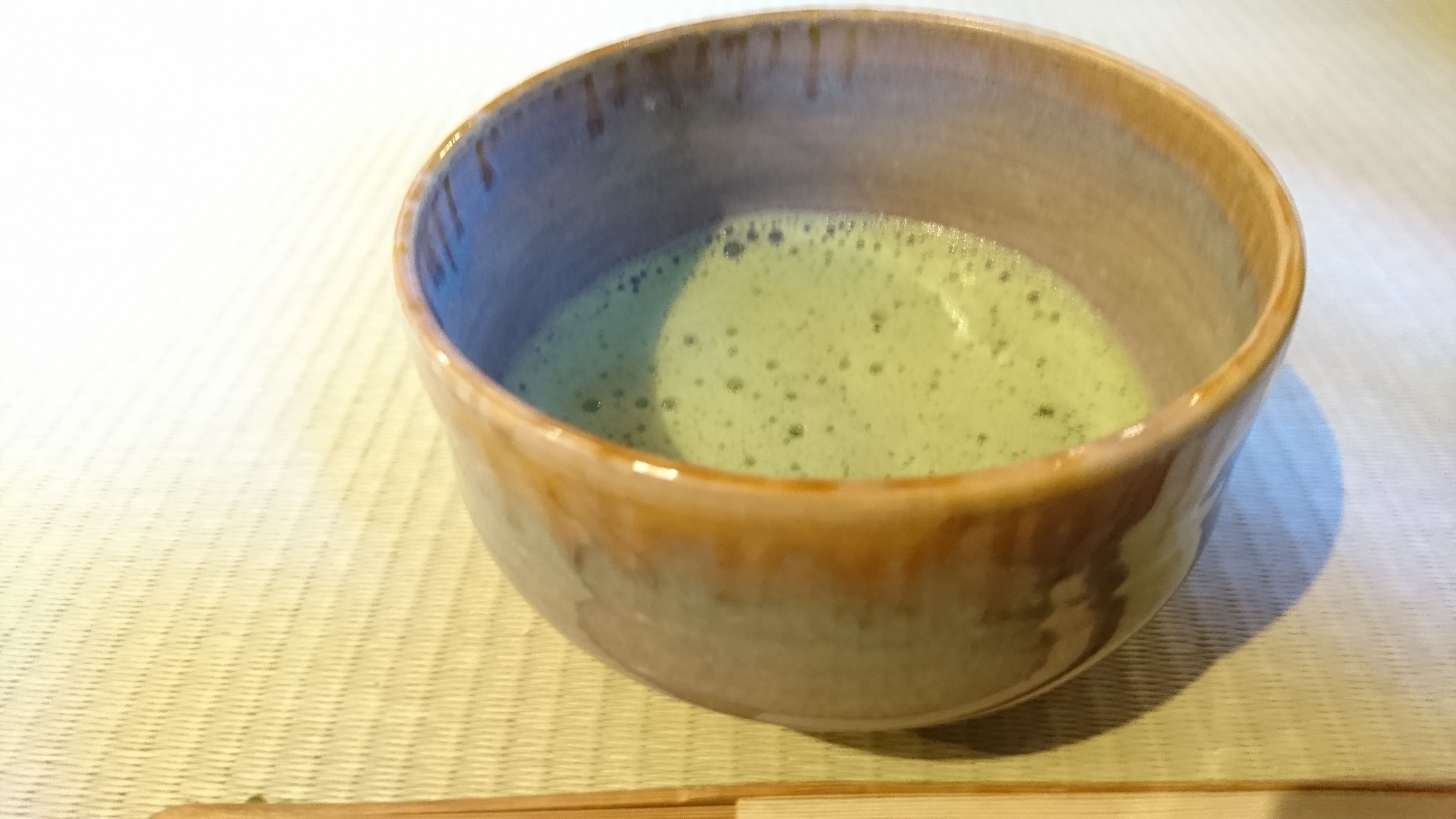 A ceramic bowl with a greenish liquid on a woven mat.