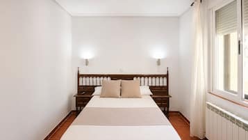 A bedroom with a wooden bed, two bedside tables, a nightstand, a window with curtains, and a radiator.