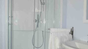 A glass-enclosed shower with a handheld showerhead, a white sink, and a towel rack.