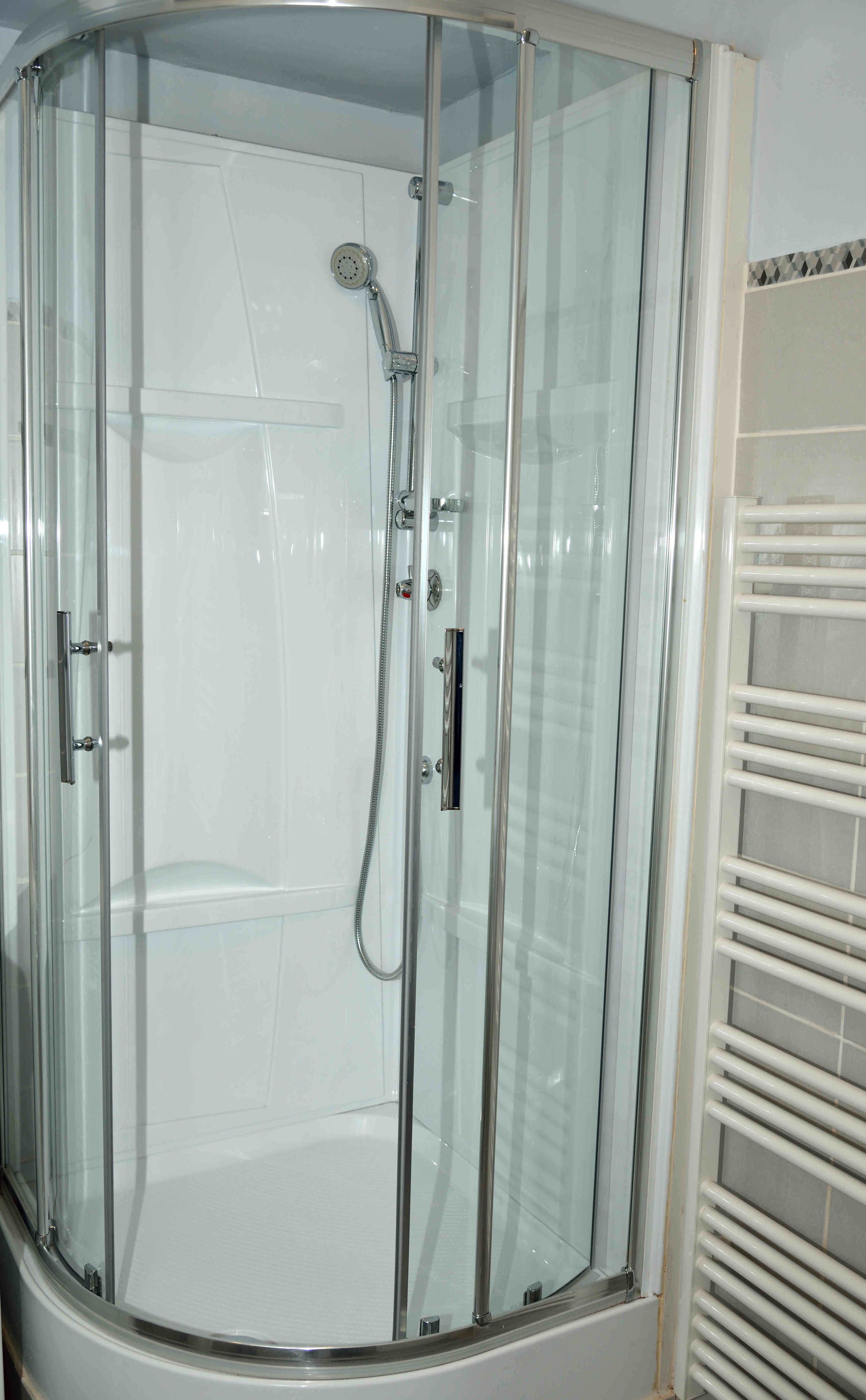 A glass-enclosed shower with a handheld showerhead and a wall-mounted faucet.