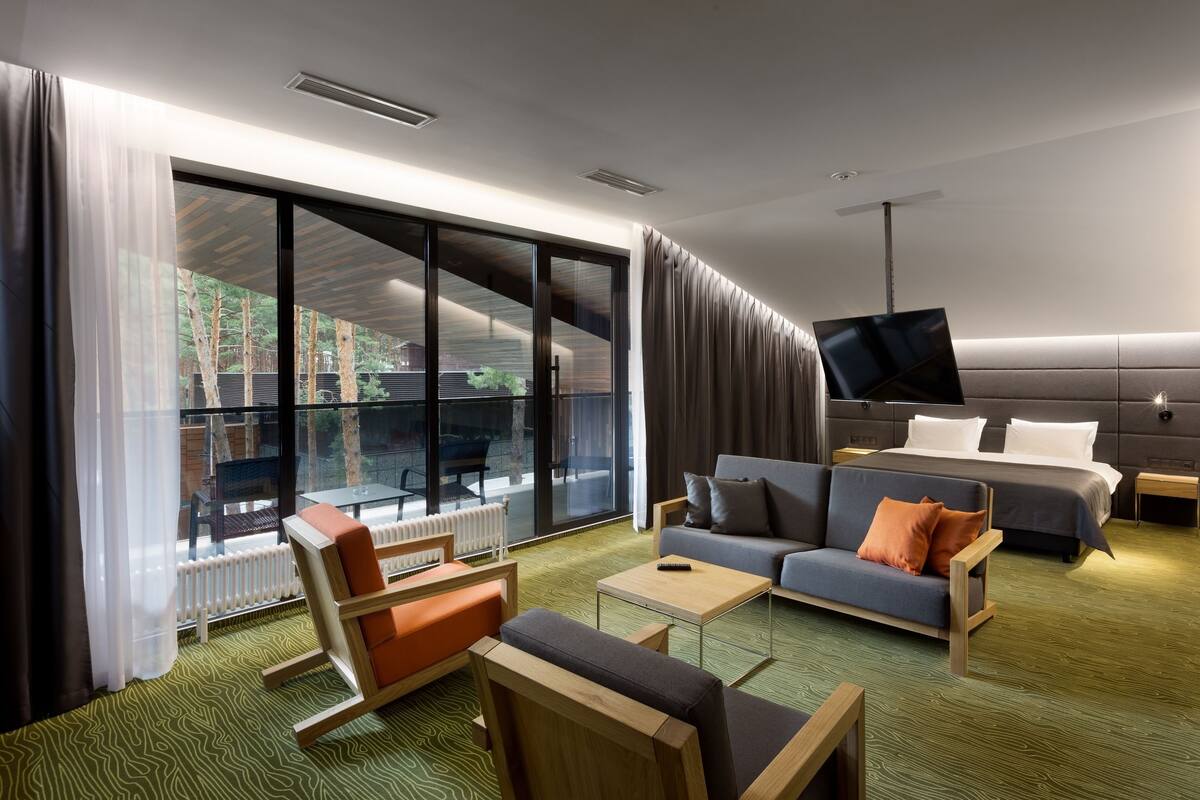 A modern hotel room with a large sliding glass door, a sofa, a bed, a TV, and a small table.