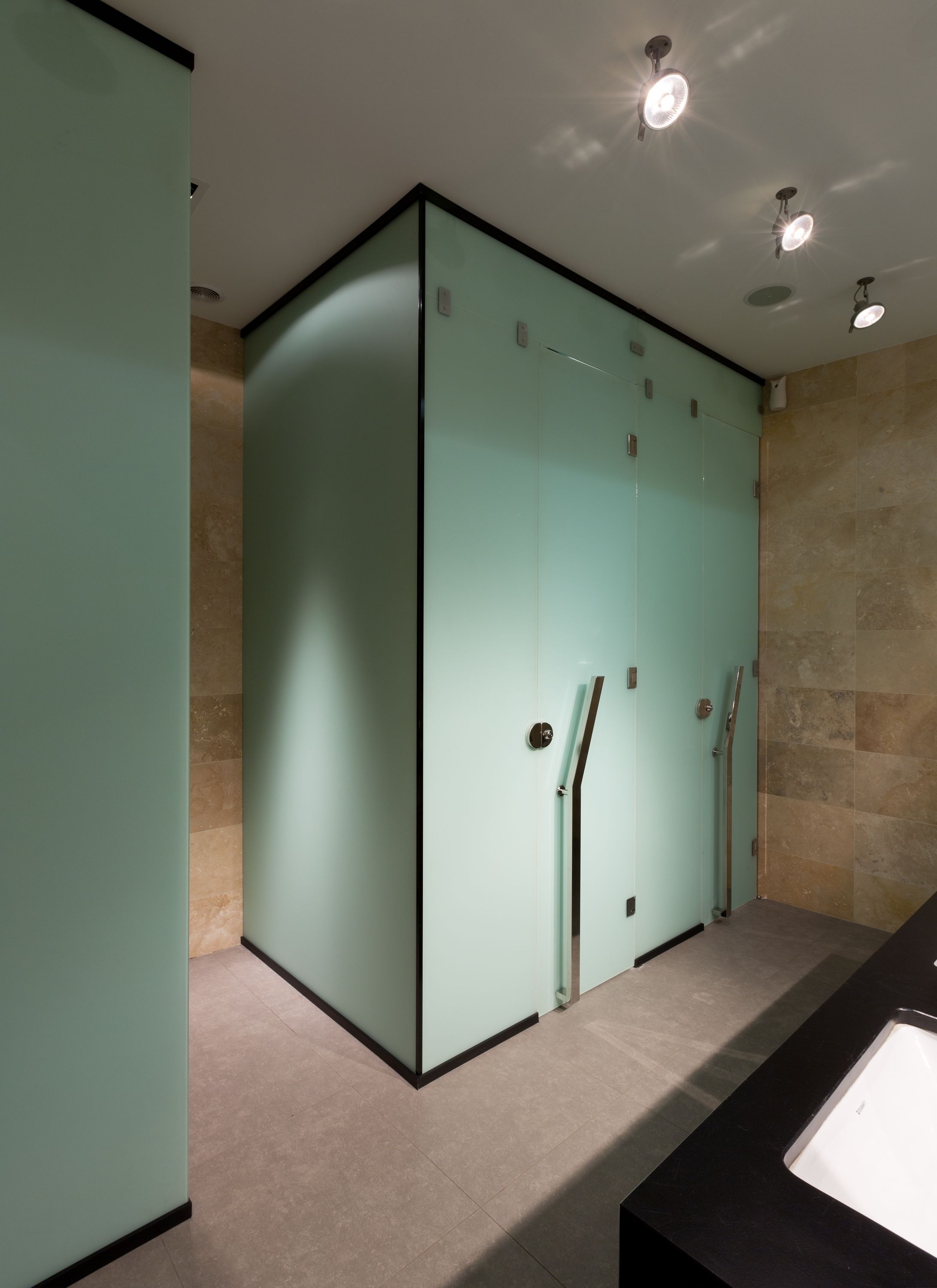 A modern bathroom with a glass shower enclosure, a black sink, and beige tiles.