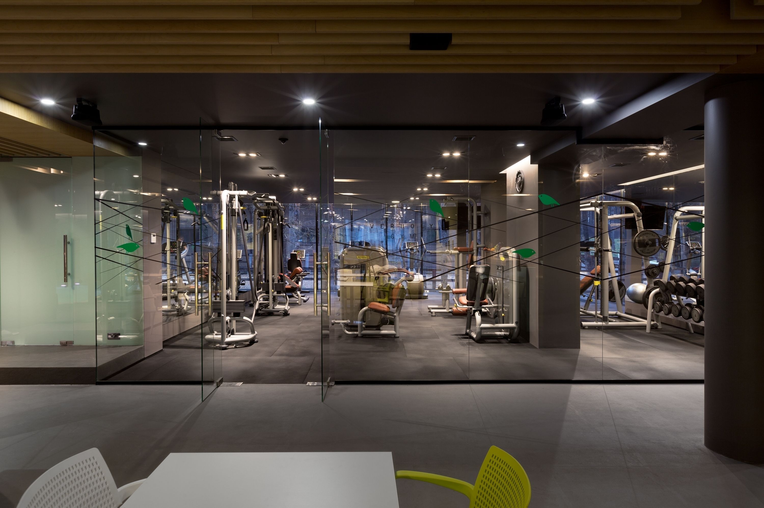 A modern gym with various exercise machines, glass walls, and a clean, well-lit interior.