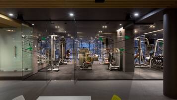 A modern gym with various exercise machines, glass walls, and a clean, well-lit interior.