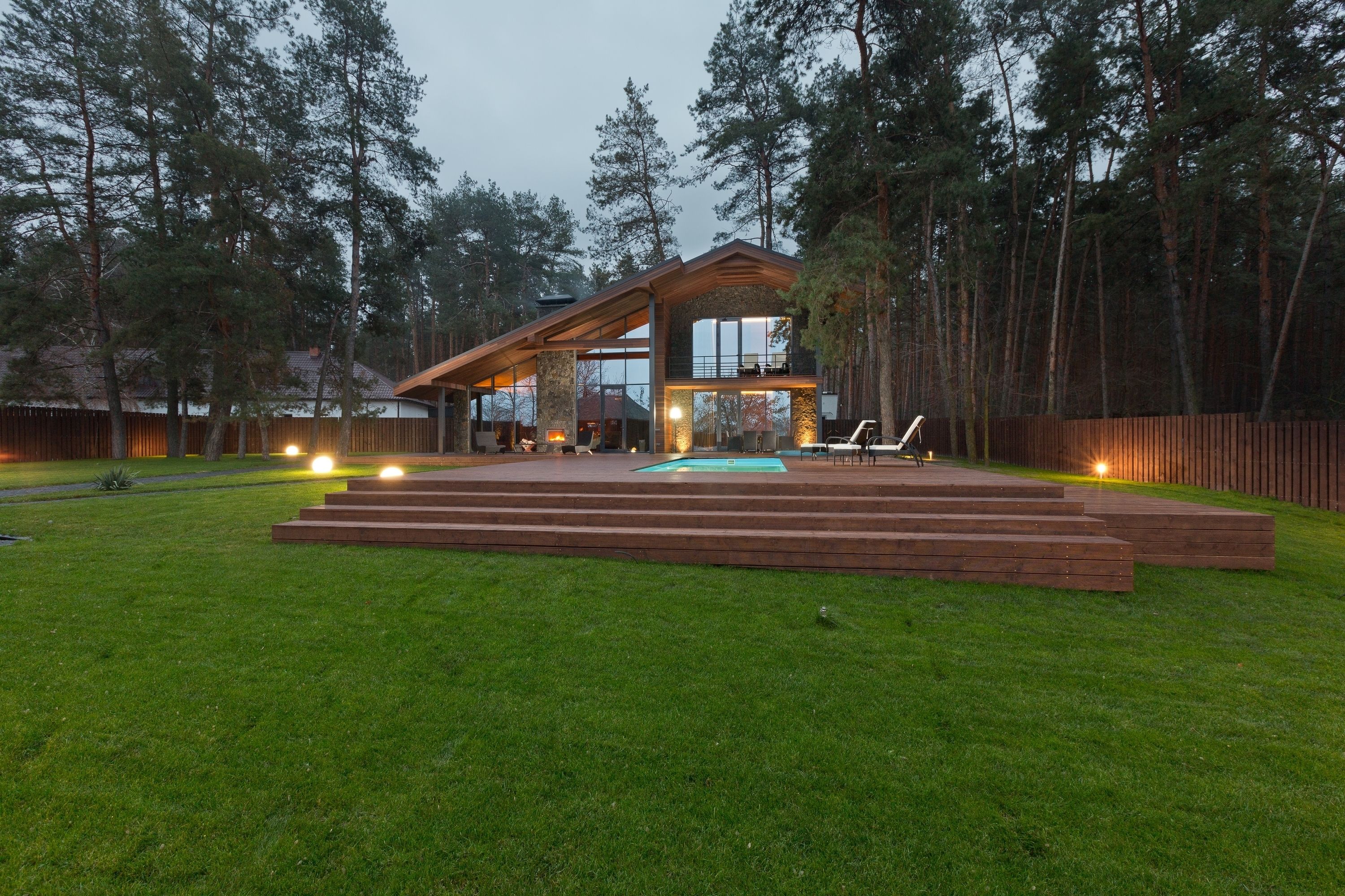 A modern house with a large deck, a swimming pool, and a wooden fence.