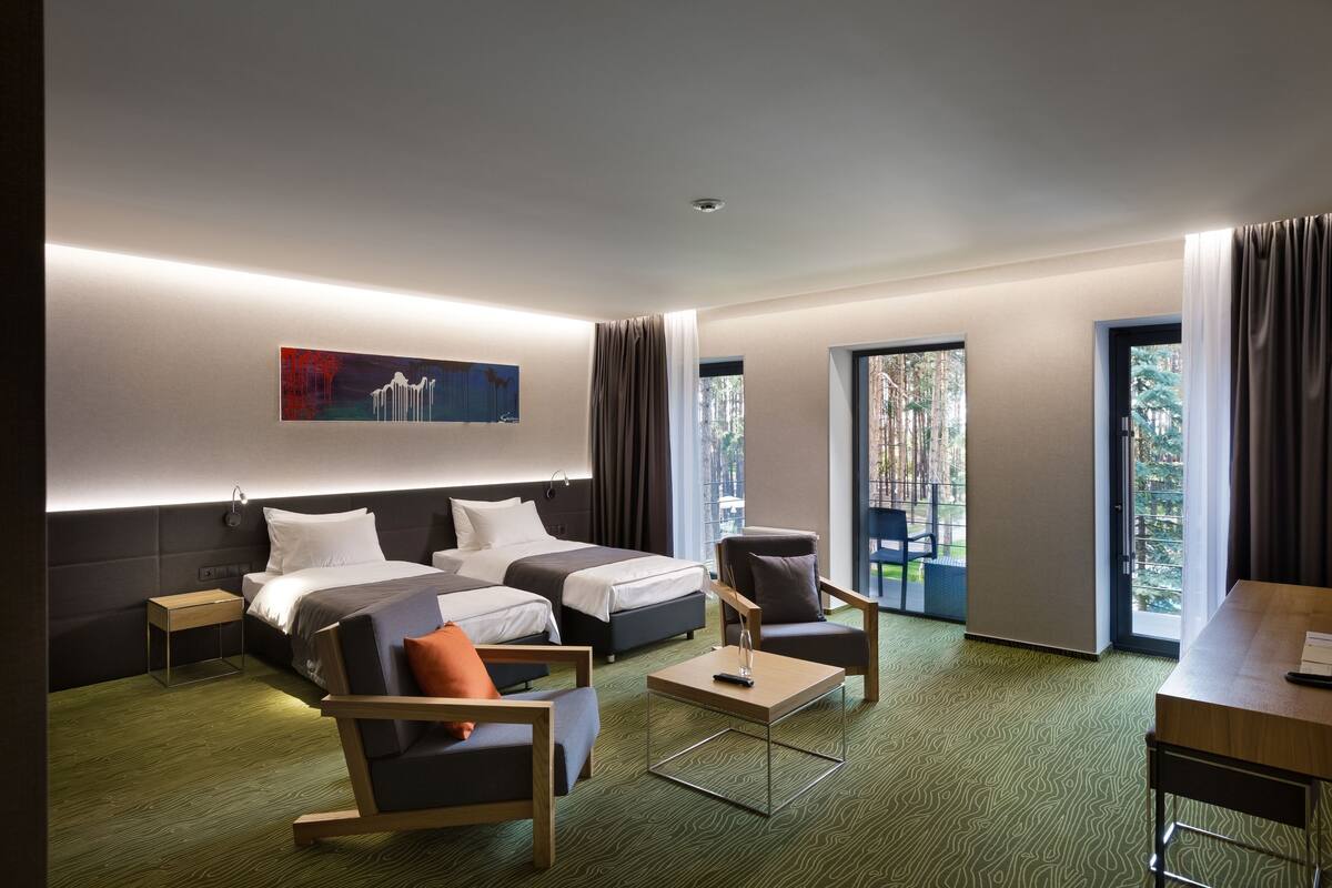 A modern hotel room with two beds, a sofa, a small table, and a desk.